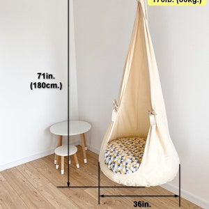May include: A white fabric hanging chair with a yellow and blue patterned cushion. The chair is suspended from the ceiling and has a weight limit of 176 pounds (80 kilograms). The chair is 71 inches (180 centimeters) tall and 36 inches (90 centimeters) wide.