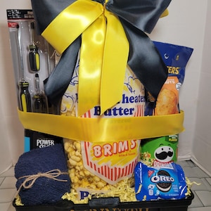 May include: A black toolbox gift basket with snacks, tools, and a blue towel. The basket is decorated with a large yellow and gray bow. The toolbox has the name "KENNETH" printed on it.