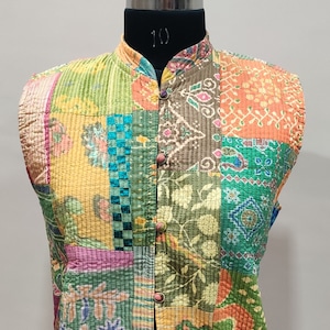May include: A sleeveless quilted vest with a patchwork design featuring various colors and patterns, including green, yellow, orange, pink, and blue. The vest has a mandarin collar and a button closure.