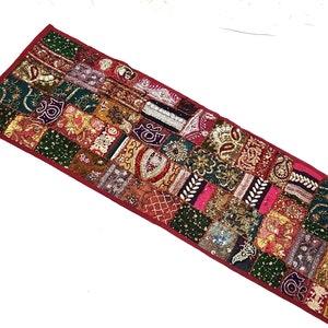 May include: A long, rectangular table runner with a patchwork design. The runner is made of various fabrics in shades of red, green, gold, and brown. It is decorated with sequins and beads.