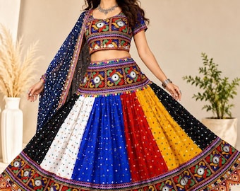 May include: A multi-colored lehenga choli set featuring a short-sleeved blouse and a voluminous skirt with vertical panels of black, white, blue, red, and yellow fabric. The garment is decorated with intricate embroidery, mirror work, and a dupatta.
