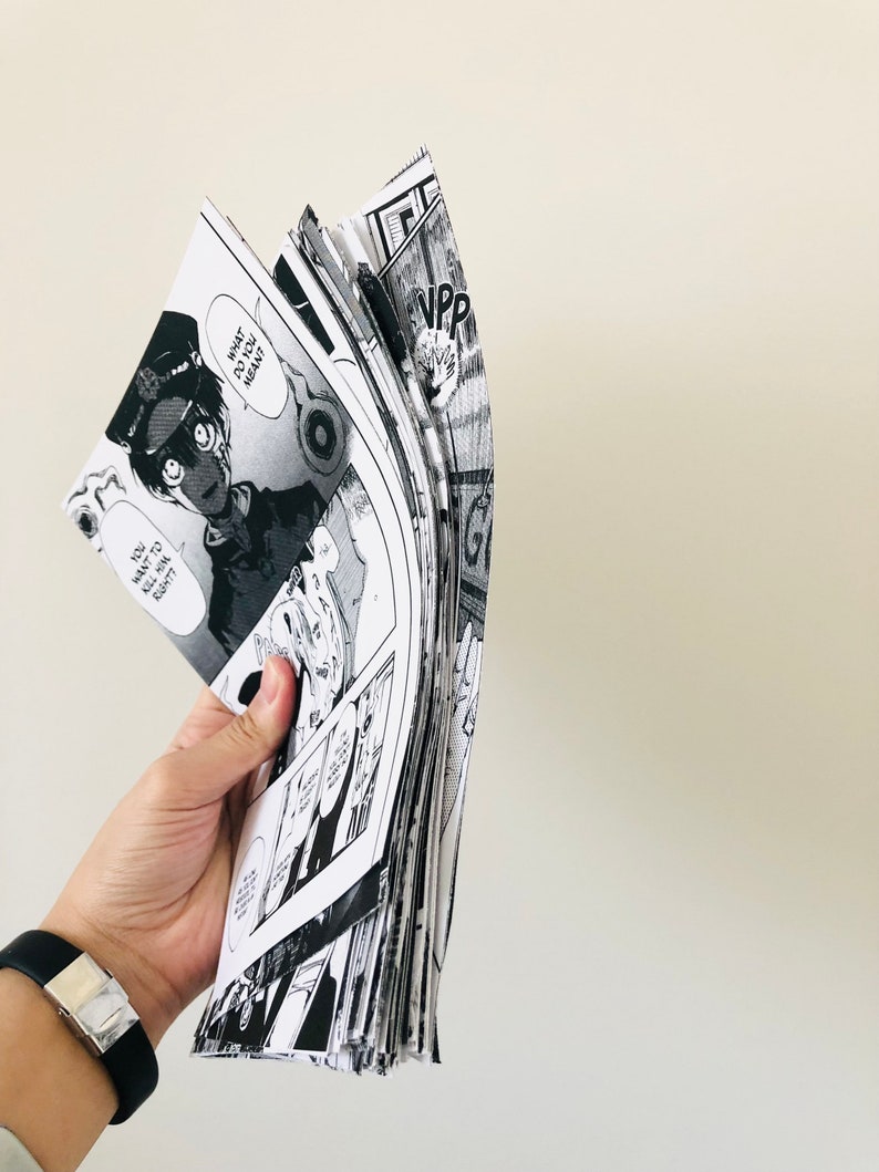 Peut inclure: Une pile de mangas en noir et blanc, tenue par une main. Les pages sont d&eacute;ploy&eacute;es, r&eacute;v&eacute;lant des cases avec des bulles de dialogue et des illustrations d&eacute;taill&eacute;es. Le texte "WHAT DO YOU MEAN?" est visible.