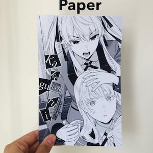 Peut inclure: Papier photo brillant avec une illustration de manga en noir et blanc. L'&oelig;uvre repr&eacute;sente deux personnages f&eacute;minins avec des expressions faciales et des coiffures d&eacute;taill&eacute;es. Le texte sur l'impression comprend "Kakegurui" et "Chapitre 83.5".