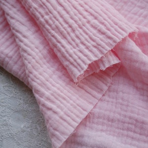 K&ouml;nnte beinhalten: Nahaufnahme eines weichen, rosa, strukturierten Stoffes. Der Stoff ist gefaltet und hat ein zerknittertes Aussehen.