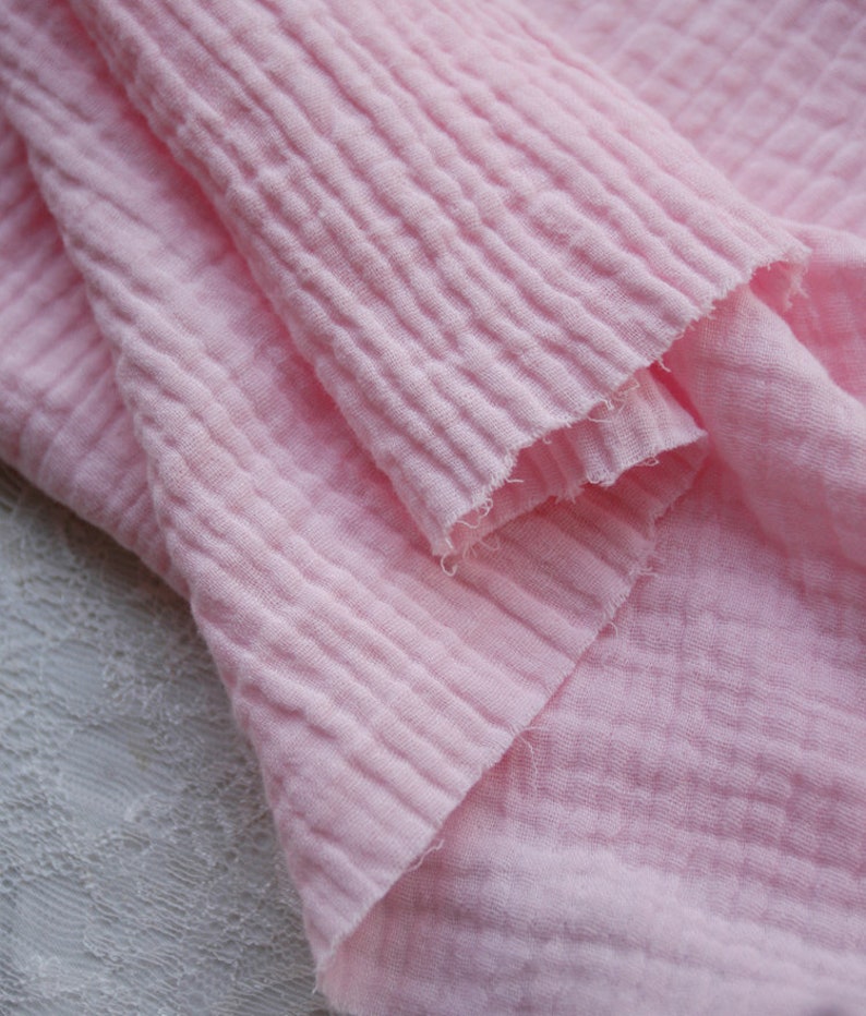 K&ouml;nnte beinhalten: Nahaufnahme eines weichen, rosa, strukturierten Stoffes. Der Stoff ist gefaltet und hat ein zerknittertes Aussehen.
