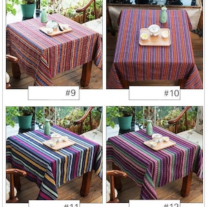 Op de afbeelding: Vier verschillende gestreepte tafelkleden in verschillende kleuren, waaronder rood, blauw, paars en geel. De tafelkleden zijn gemaakt van geweven stof en hebben een casual, rustieke uitstraling. Elk tafelkleed wordt getoond op een houten tafel met een theepot en theekopjes erop.