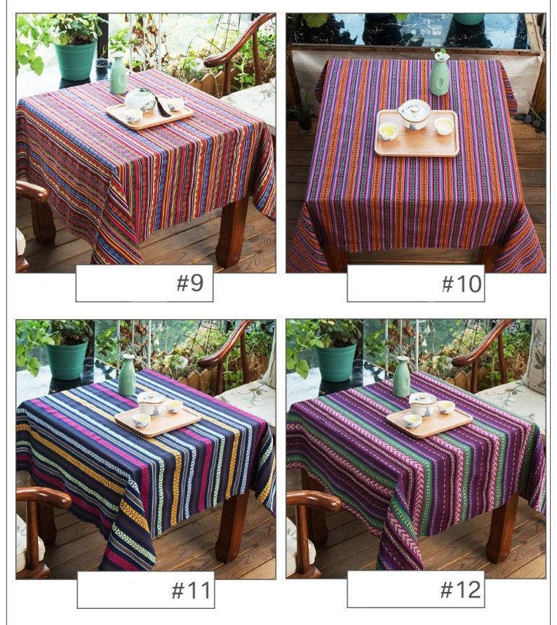 Op de afbeelding: Vier verschillende gestreepte tafelkleden in verschillende kleuren, waaronder rood, blauw, paars en geel. De tafelkleden zijn gemaakt van geweven stof en hebben een casual, rustieke uitstraling. Elk tafelkleed wordt getoond op een houten tafel met een theepot en theekopjes erop.