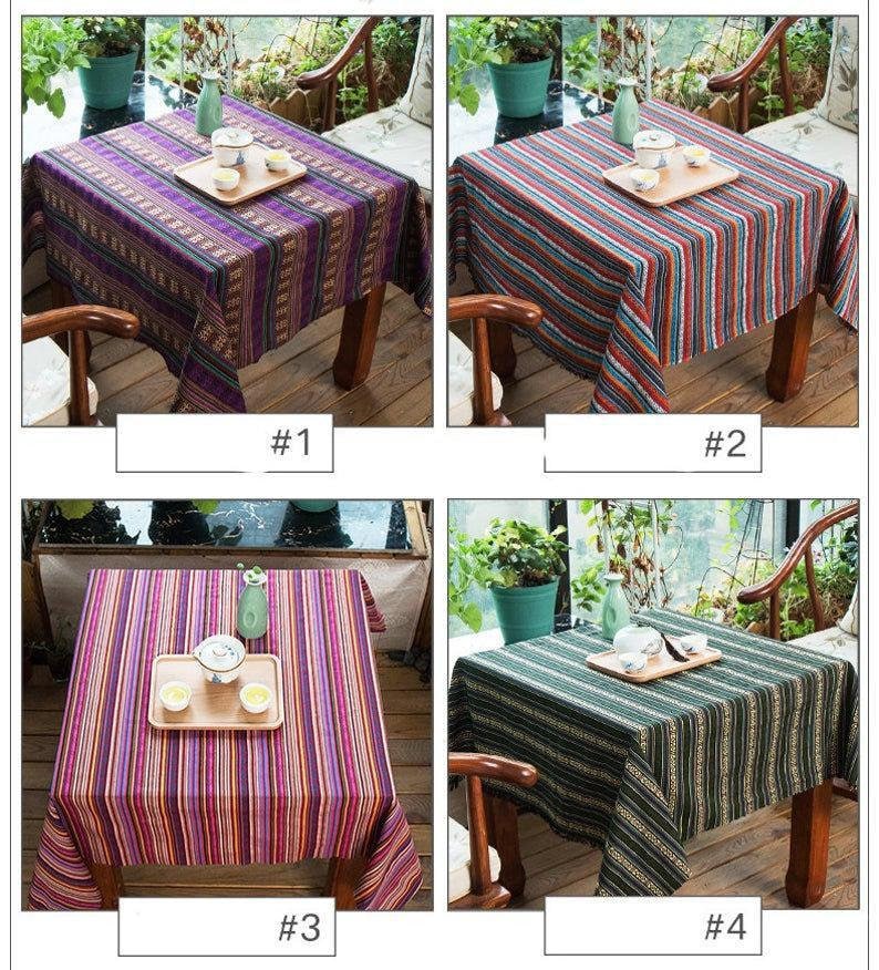 Op de afbeelding: Vier verschillende gestreepte tafelkleden in verschillende kleuren, waaronder paars, rood, blauw en groen. De tafelkleden zijn gemaakt van geweven stof en hebben een eenvoudig, modern ontwerp.
