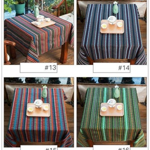 Op de afbeelding: Vier verschillende gestreepte tafelkleden in verschillende kleuren, waaronder blauw, groen, rood en zwart. Elk tafelkleed ligt op een tafel met een houten frame en heeft een klein houten dienblad met twee theekopjes en een theepot.