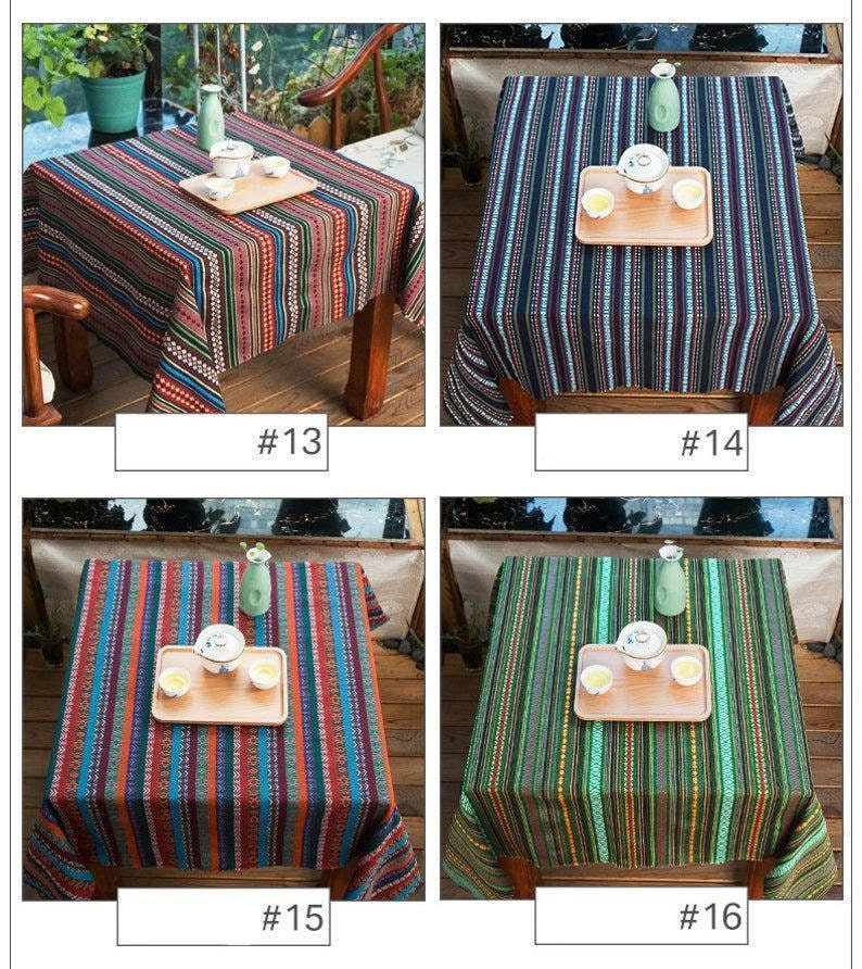 Op de afbeelding: Vier verschillende gestreepte tafelkleden in verschillende kleuren, waaronder blauw, groen, rood en zwart. Elk tafelkleed ligt op een tafel met een houten frame en heeft een klein houten dienblad met twee theekopjes en een theepot.