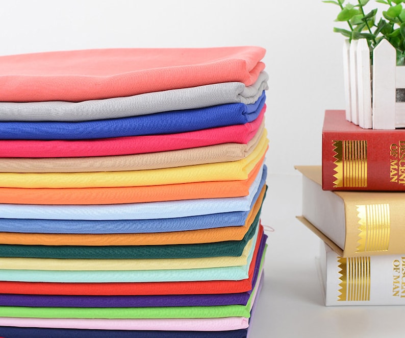 May include: A stack of 18 different colored fabric swatches. The swatches are arranged in a rainbow pattern, with the colors ranging from pink to purple.