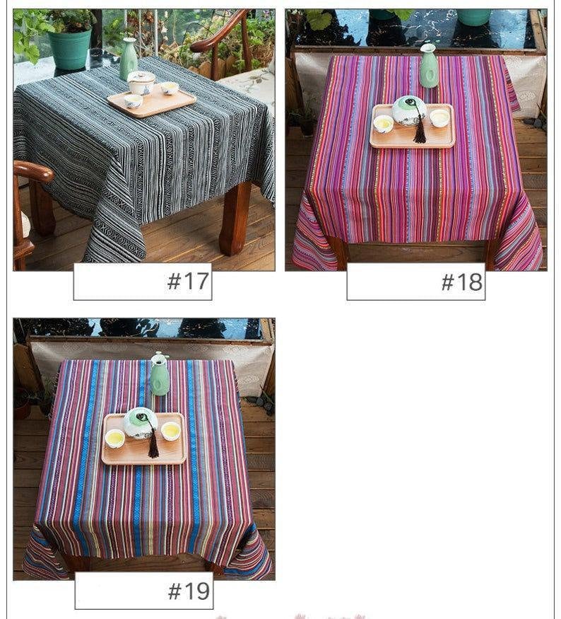 Op de afbeelding: Drie verschillende gestreepte tafelkleden in zwart-wit, roze en paars, en blauw en rood. Elk tafelkleed wordt getoond op een houten tafel met een theepot en theekopjes op een houten dienblad.