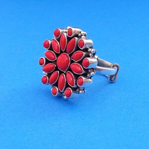 Puede incluir: Un anillo de plata con un dise&ntilde;o de flor roja. La flor tiene 14 p&eacute;talos y una piedra central.