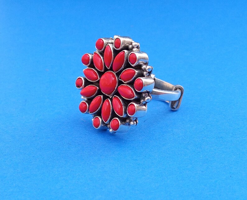 Puede incluir: Un anillo de plata con un dise&ntilde;o de flor roja. La flor tiene 14 p&eacute;talos y una piedra central.