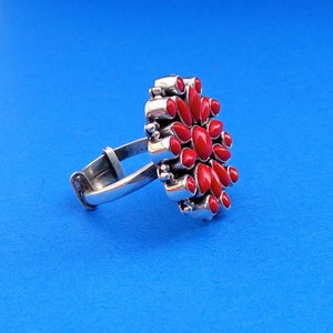 Puede incluir: Un anillo de plata con un dise&ntilde;o de flor de coral rojo. El anillo tiene una banda simple y un gran dise&ntilde;o de flor detallado con muchas piedras de coral rojo.