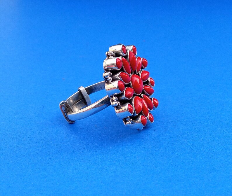 Puede incluir: Un anillo de plata con un dise&ntilde;o de flor de coral rojo. El anillo tiene una banda simple y un gran dise&ntilde;o de flor detallado con muchas piedras de coral rojo.