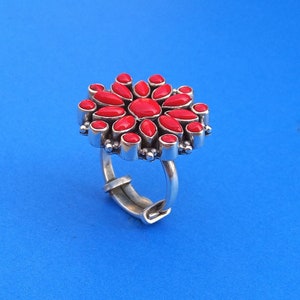 Puede incluir: Un anillo de plata con un dise&ntilde;o de flor roja. La flor est&aacute; hecha de muchas piedras rojas peque&ntilde;as.