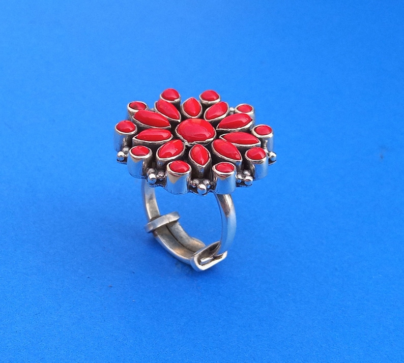 Puede incluir: Un anillo de plata con un dise&ntilde;o de flor roja. La flor est&aacute; hecha de muchas piedras rojas peque&ntilde;as.