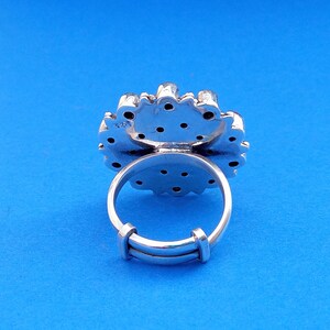Puede incluir: Anillo de plata con un dise&ntilde;o floral y una banda de plata. El anillo est&aacute; engastado con peque&ntilde;as piedras redondas.