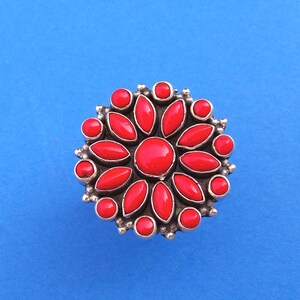 Puede incluir: Un anillo de plata con un dise&ntilde;o de flor roja. La flor tiene 12 p&eacute;talos y una piedra central.