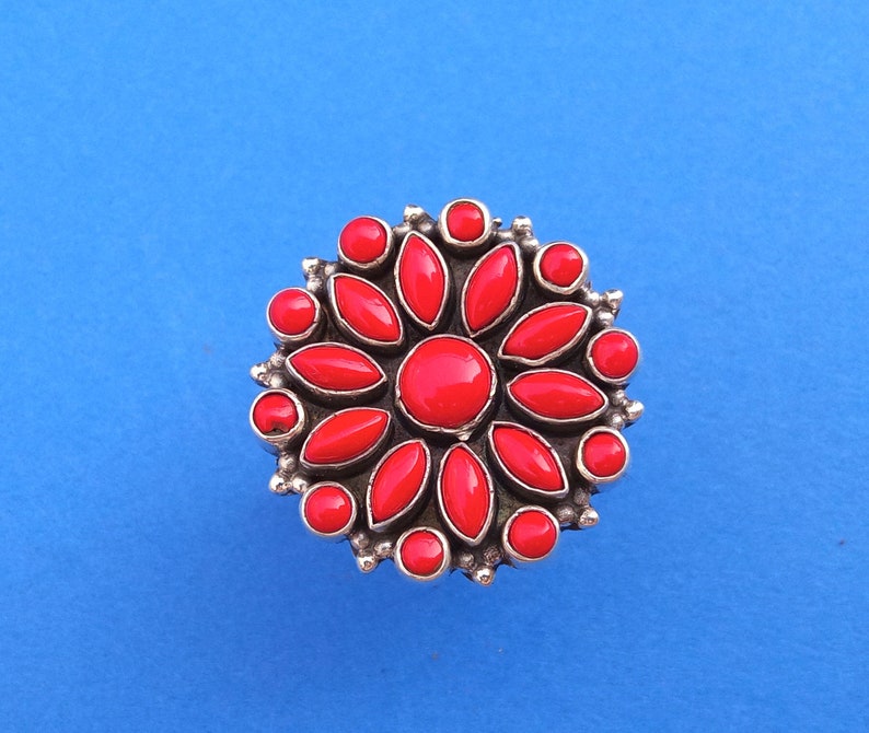 Puede incluir: Un anillo de plata con un dise&ntilde;o de flor roja. La flor tiene 12 p&eacute;talos y una piedra central.