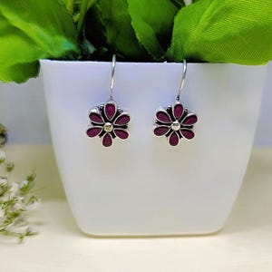 以下が含まれることがあります： 花柄のシルバー製のドロップイヤリングのペア。花は紫で、中心は金色です。