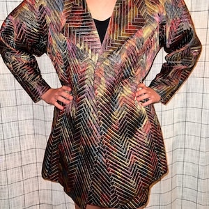 May include: A long-sleeved jacket with a geometric pattern in shades of red, gold, black, and blue. The jacket has a V-neck and a loose fit.