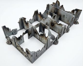 May include: A miniature model of a ruined building with gray walls, jagged edges, and dark scorch marks. The structure features multiple interior rooms, open doorways, and textured debris at the base, simulating a war-torn urban environment.