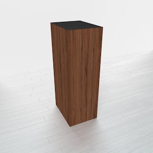 May include: A tall, rectangular wooden display stand with a black top. The stand has a wood grain pattern and is made of a dark brown wood.