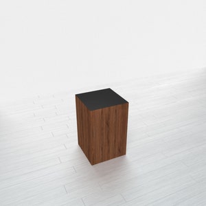 May include: A square wooden side table with a dark brown finish and a black top. The table has a natural wood grain pattern and is designed with a simple, modern aesthetic. The table is approximately 20 inches tall.