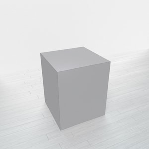 May include: A solid, gray cube-shaped object. The cube is positioned on a white, wood-planked surface. The background is a plain white wall. The cube's edges are clearly defined, and it appears to be made of a solid material.