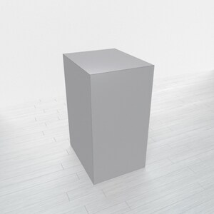 May include: A gray, rectangular pedestal or platform, likely made of wood or plastic, sits on a white wood floor. It is a simple, blank surface that could be used for displaying products or artwork.