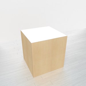 May include: A square wooden display stand with a light wood grain finish and a white top. The stand is a cube shape and is suitable for displaying products.