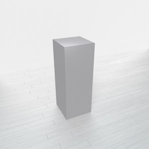 May include: A gray, rectangular pedestal or display stand with a smooth surface. The stand is on a white wood floor.