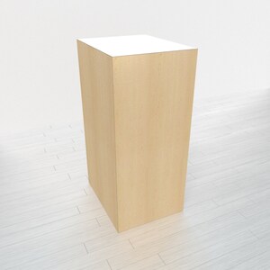 May include: A light wood display stand with a white top. The stand is rectangular and has a smooth surface.