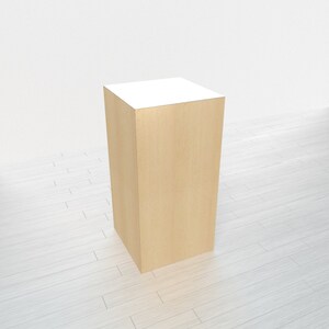 May include: A light wood square pedestal with a white top. The pedestal is sitting on a white wood floor.