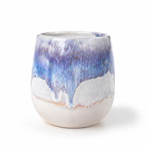 Op de afbeelding: Een keramische tumbler met een afgeronde basis en een brede opening. Het bovenste deel van de tumbler heeft een blauw en paars glazuur dat over een witte basis druipt. De tumbler is neutraal van kleur en heeft een gladde afwerking.