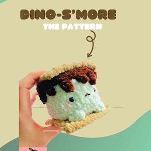 May include: A crocheted plush toy shaped like a s'more. The toy is green, brown, and tan. The toy is being held in a hand. The text "Dino-S'more The Pattern" is at the top of the image.