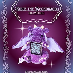 Op de afbeelding: Een paarse pluche draak die een tablet vasthoudt, met de tekst "Fable the Bookdragon" en "The Pattern" erboven. De draak heeft witte vleugels en gele hoorns. De achtergrond is een verloop van paars en blauw.