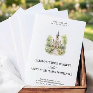 May include: White wedding programs with text: "WELCOME TO THE WEDDING OF CHARLOTTE ROSE BENNETT And ALEXANDER JAMES WHITMORE." The programs feature a watercolour illustration of a church. The programs are in a wooden box.
