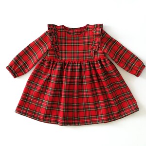 May include: Red and green plaid dress with long sleeves and a ruffled neckline.