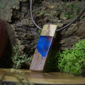 May include: A wooden pendant with a blue and purple resin inlay. The pendant is attached to a brown cord.