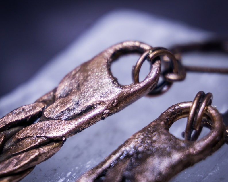 May include: Close-up of a pair of bronze earrings with a textured, braided design. The earrings have a unique, organic look and feel.