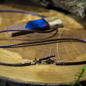 May include: A brown leather cord necklace with a wooden pendant featuring a blue and white resin inlay. The pendant has a natural wood grain pattern and a dark brown finish.