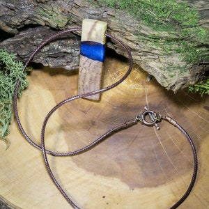 May include: A brown leather cord necklace with a wooden pendant featuring a blue and white resin inlay.