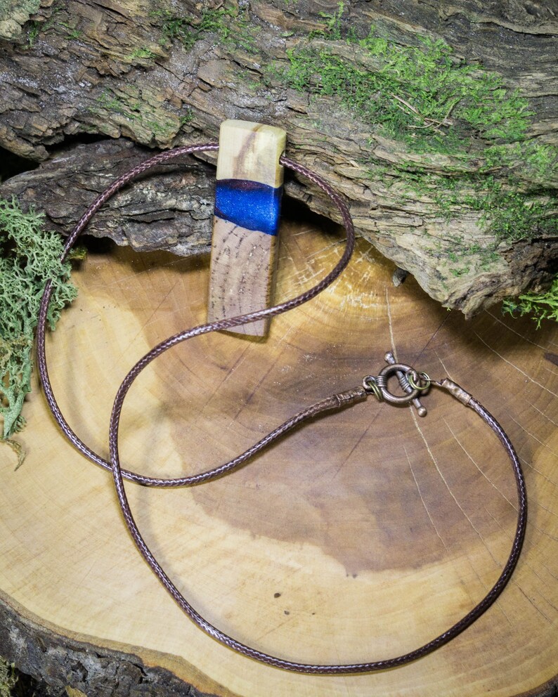 May include: A brown leather cord necklace with a wooden pendant featuring a blue and white resin inlay.