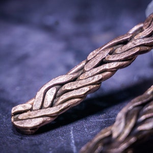 May include: Close-up of a braided copper bracelet with a woven pattern. The bracelet is made of multiple strands of copper wire that are intertwined to create a complex design.
