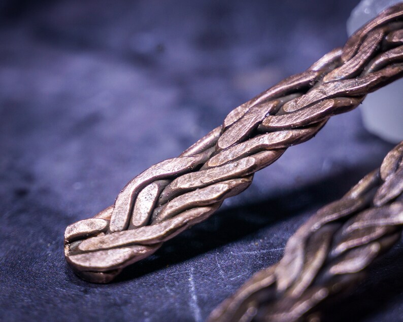 May include: Close-up of a braided copper bracelet with a woven pattern. The bracelet is made of multiple strands of copper wire that are intertwined to create a complex design.