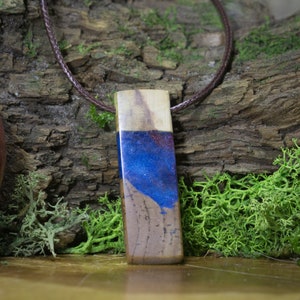 May include: A wooden pendant with a blue and purple resin inlay. The pendant is hanging from a brown leather cord.