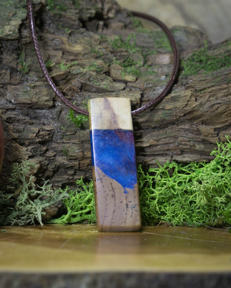 May include: A wooden pendant with a blue and purple resin inlay. The pendant is hanging from a brown leather cord.